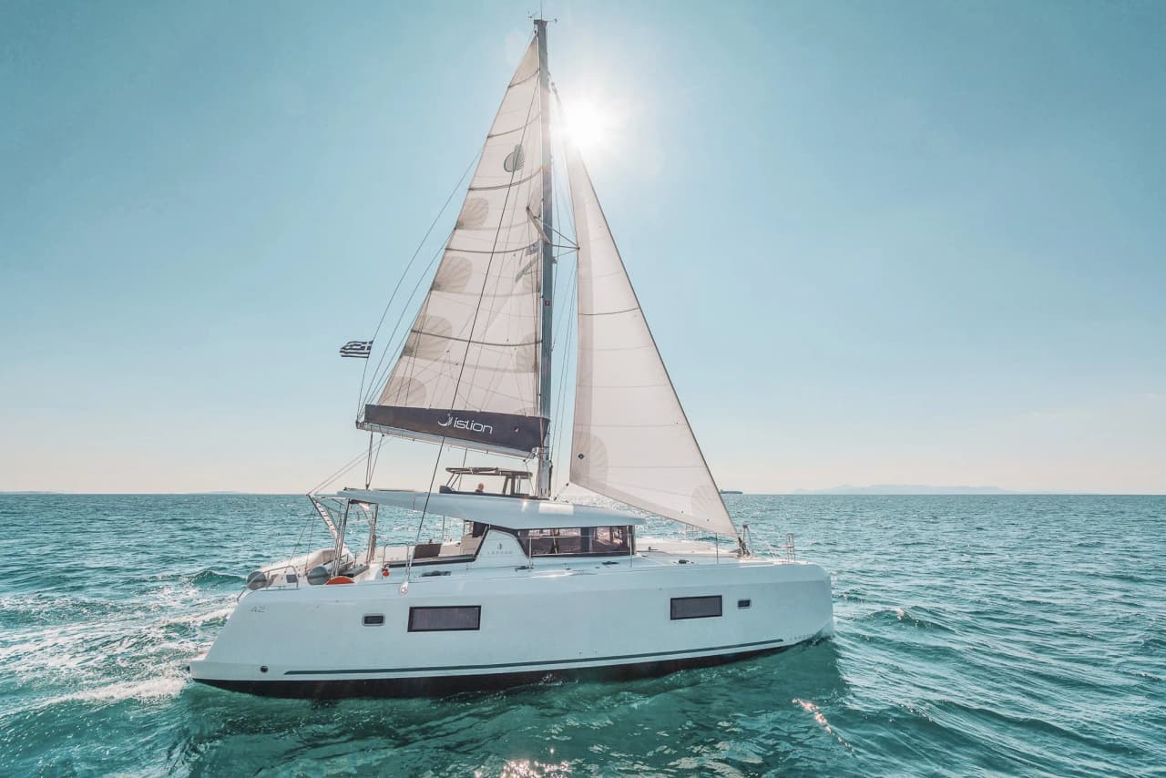 Catamaran à voile naviguant sur des eaux turquoise sous un ciel ensoleillé, invitation au voyage.