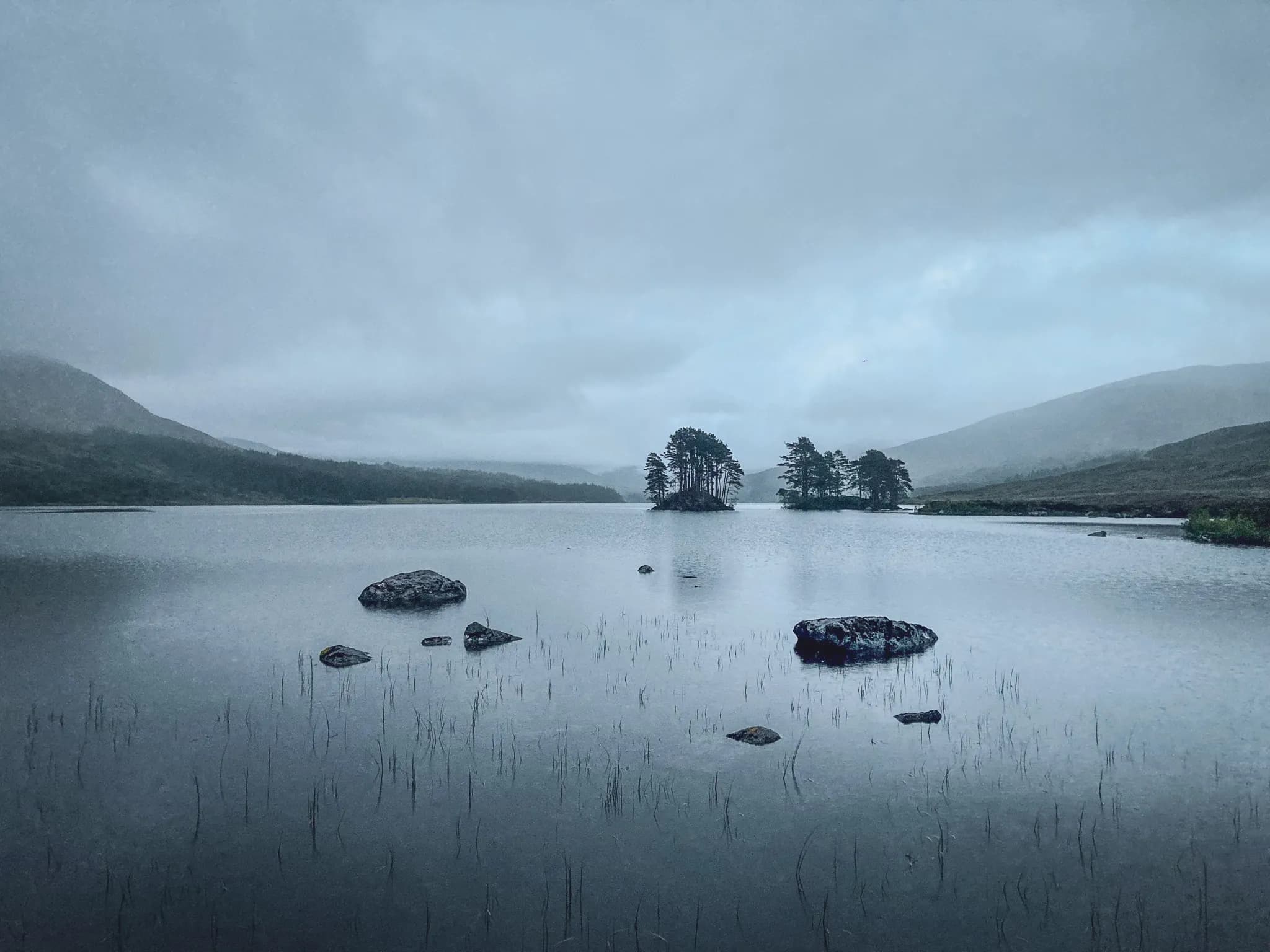 Een vredig hooglandmeer, omringd door bergen onder een bewolkte hemel, die avontuur belooft.