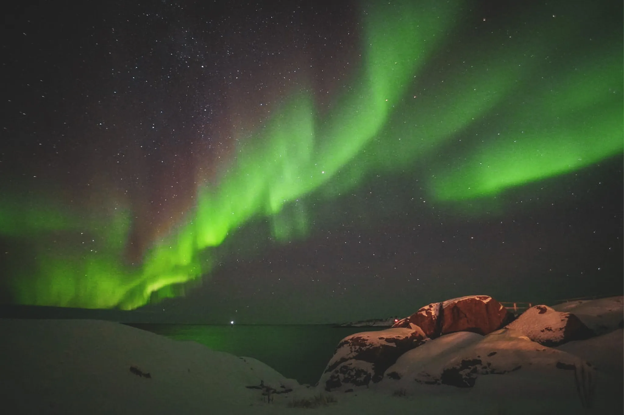 The magical Aurora Borealis lights up the starry sky above the snow-covered fjords of Senja.