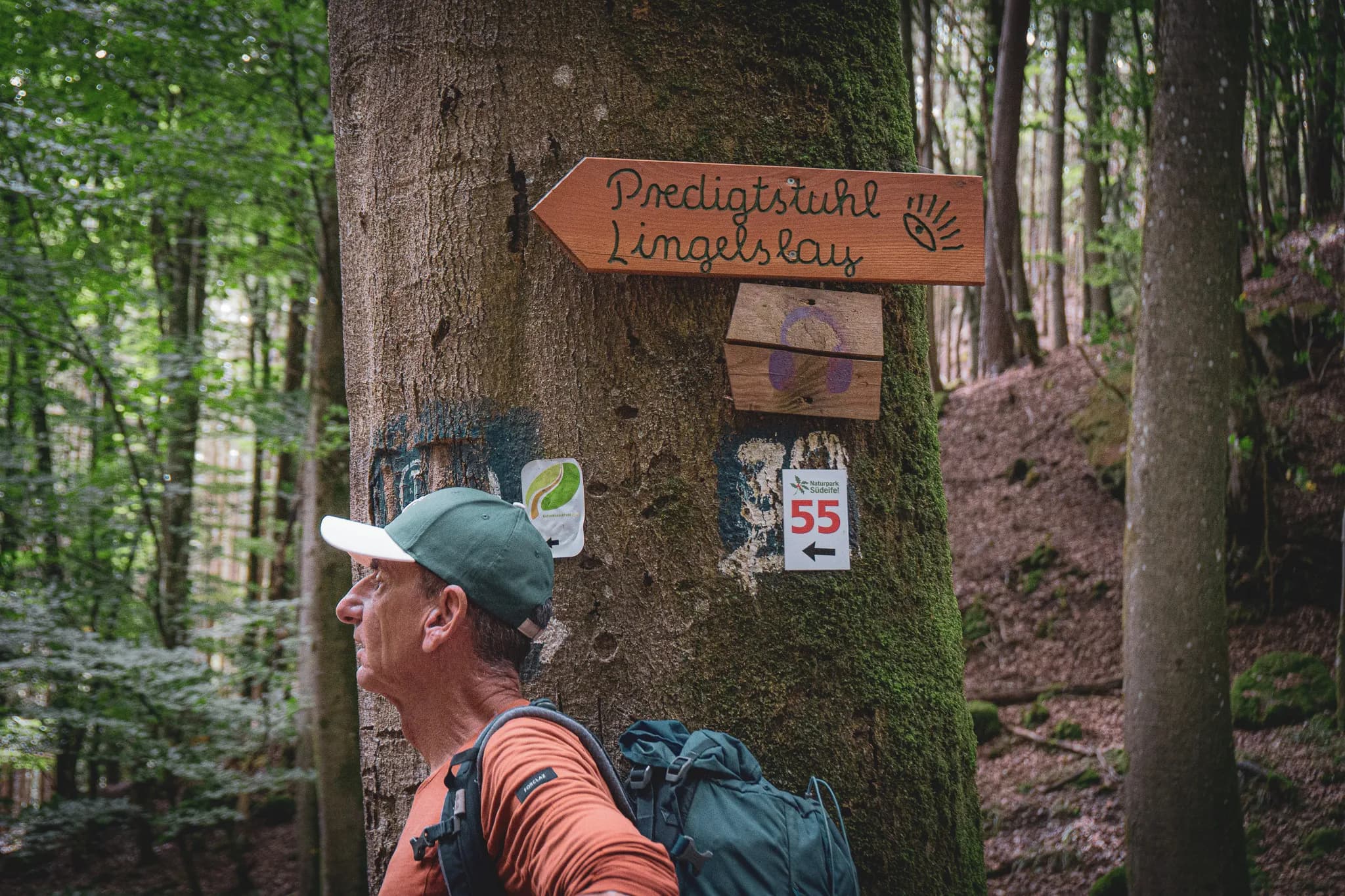 Wandelende man in een Luxemburgs bos, voor een rustiek wandelbord.
