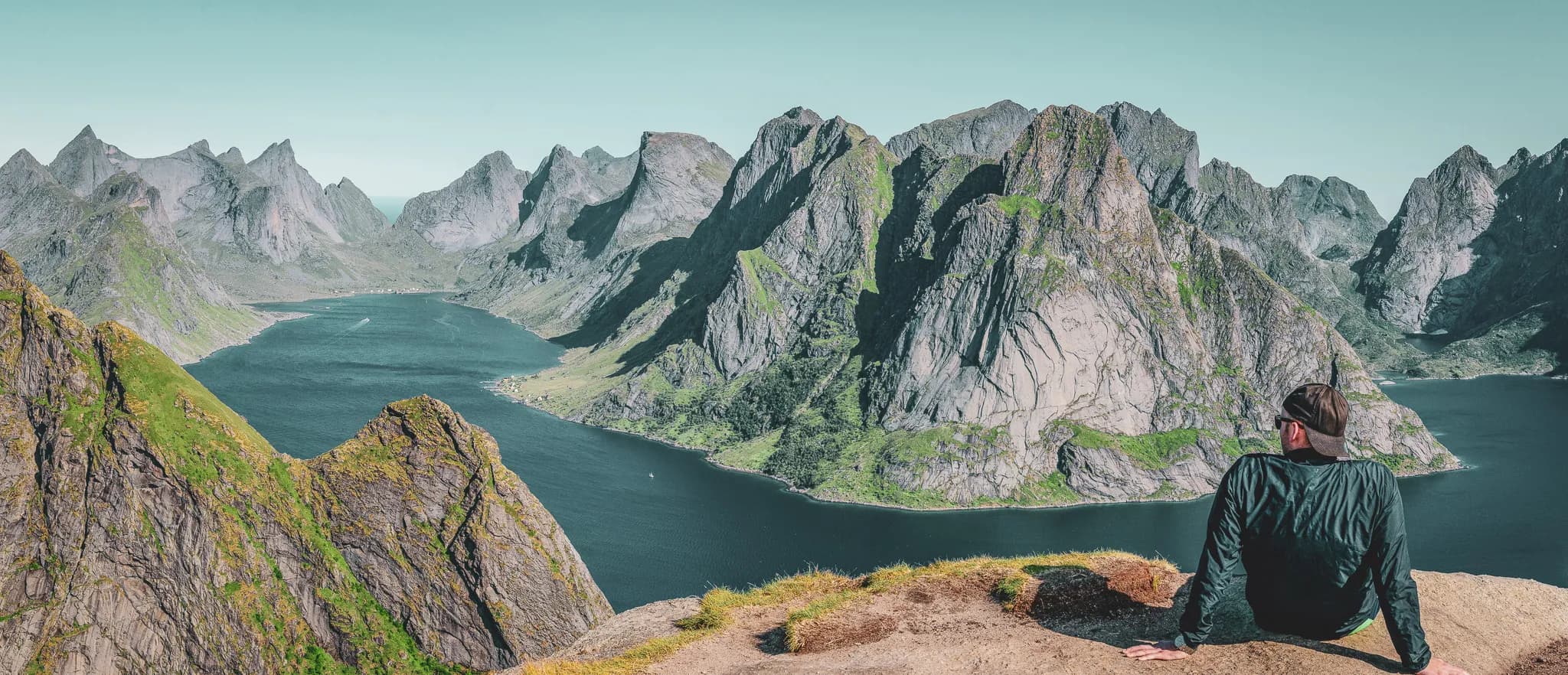A man contemplating majestic mountains and a serene fjord under the midnight sun.