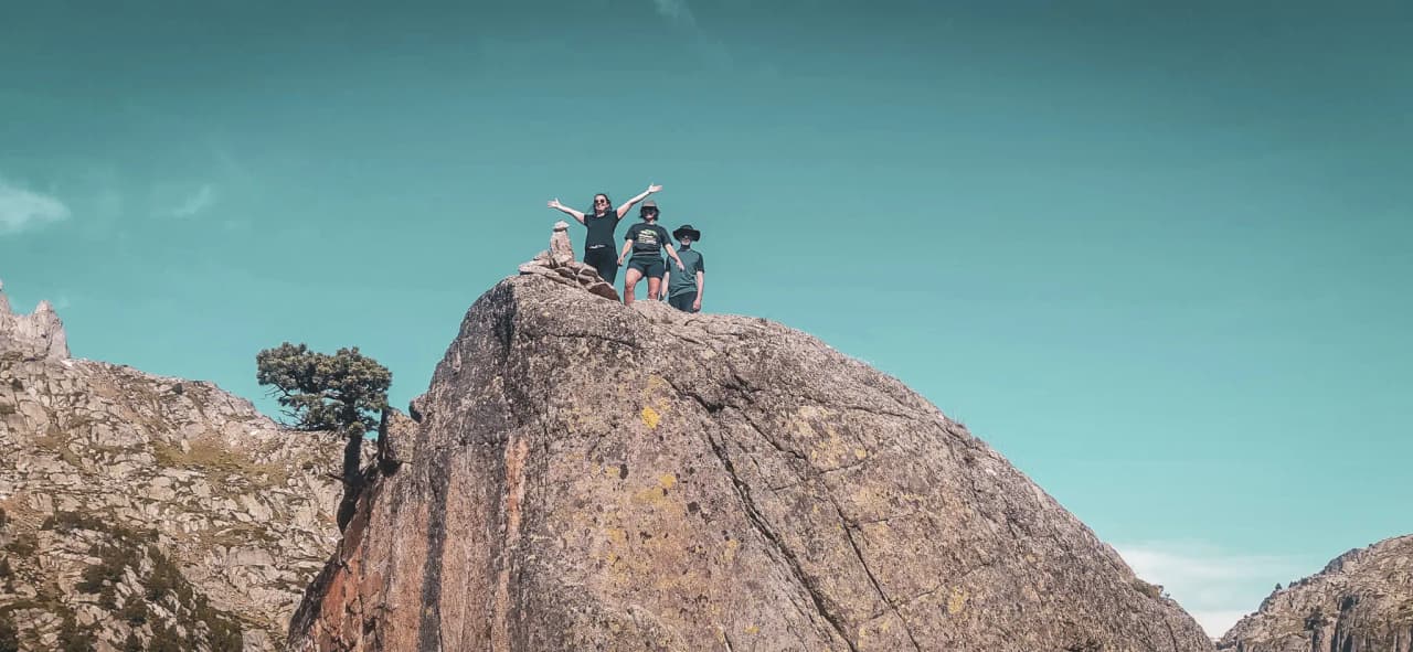 Three jubilant people on top of a rock, overlooking a dazzling mountain landscape.
