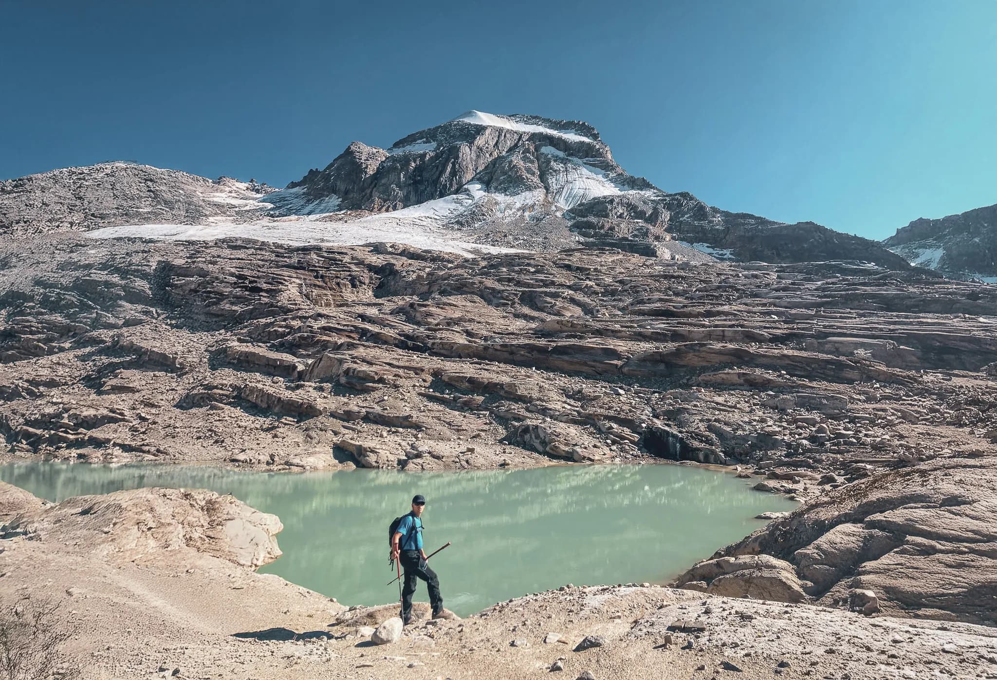 Een man poseert bij een bergmeer met de top van Gran Paradiso op de achtergrond in Italië. Het spiegelende water en de imposante berg maken het landschap adembenemend.