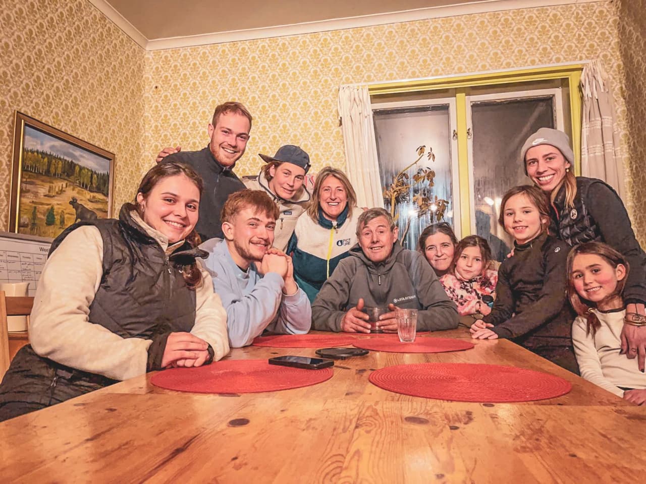 Een lachende groep rond een houten tafel in een gezellig Laplands chalet, klaar voor avontuur.