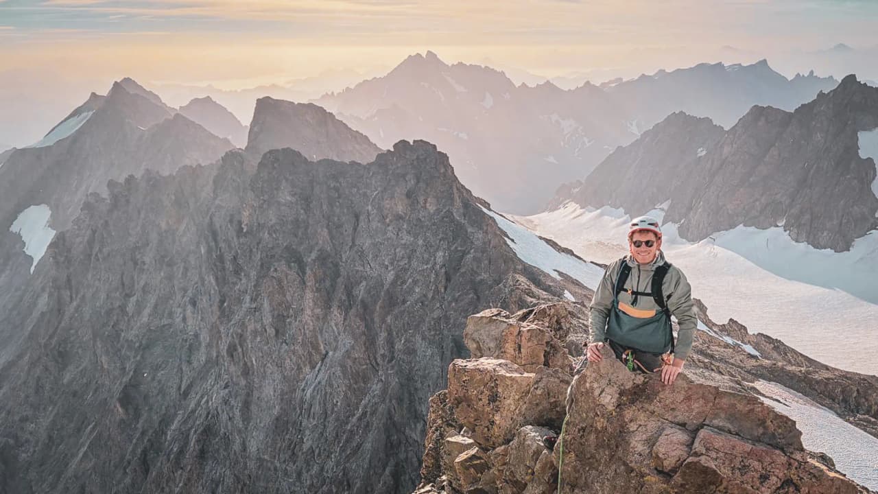 Alpiniste souriant au sommet d'une montagne des Écrins, entouré de paysages grandioses.
