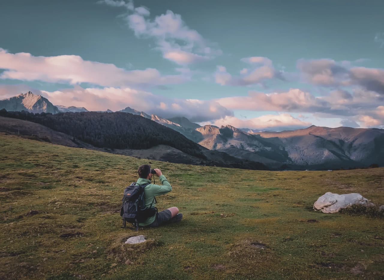 Randonneur contemplant les majestueuses montagnes des Pyrénées au coucher du soleil.