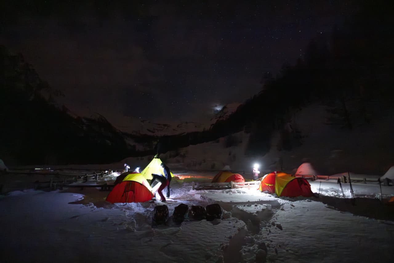 Kleurrijke tenten, verlicht onder een sterrenhemel: de betoverende sfeer van een nacht in de bergen.