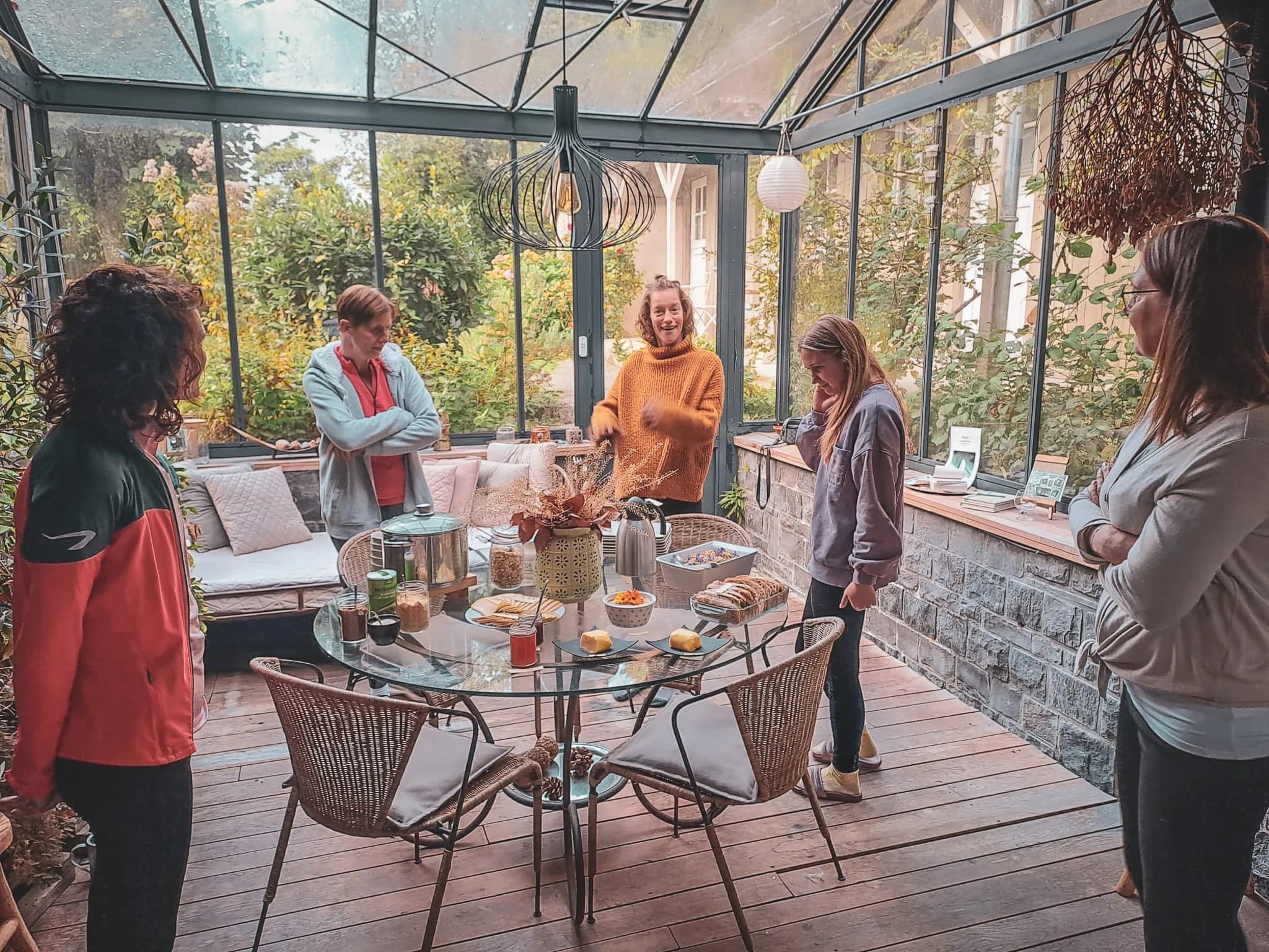 A bright, welcoming space, with large windows offering views of the surrounding greenery. A group of five people stand around a glass table, sharing a convivial moment. One of the people, dressed in a