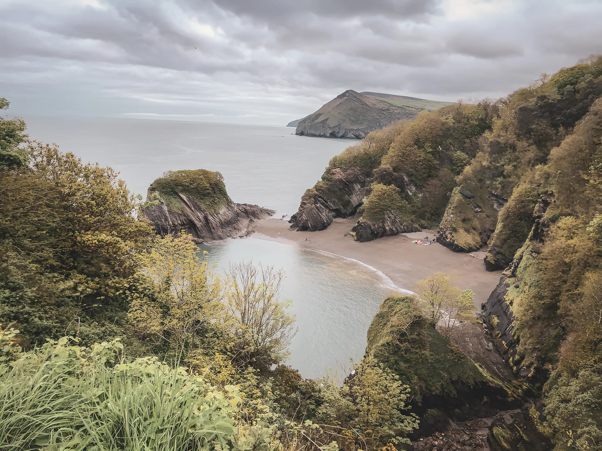 Côte sauvage galloise avec plages cachées, falaises verdoyantes et ciel nuageux. Un paradis à explorer.