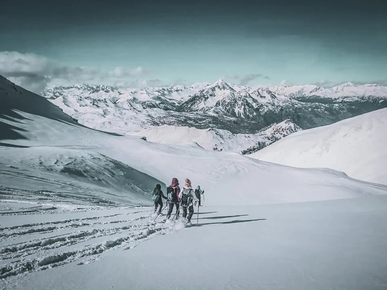 A group of hikers venture into a snow-covered Alpine landscape between majestic peaks.