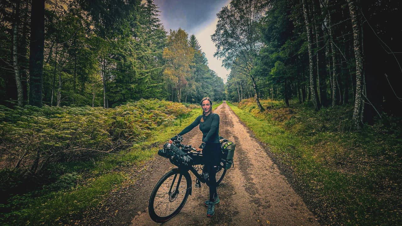 Een glimlachende vrouw op een bospad, klaar voor een fietsavontuur in de Hoge Venen.