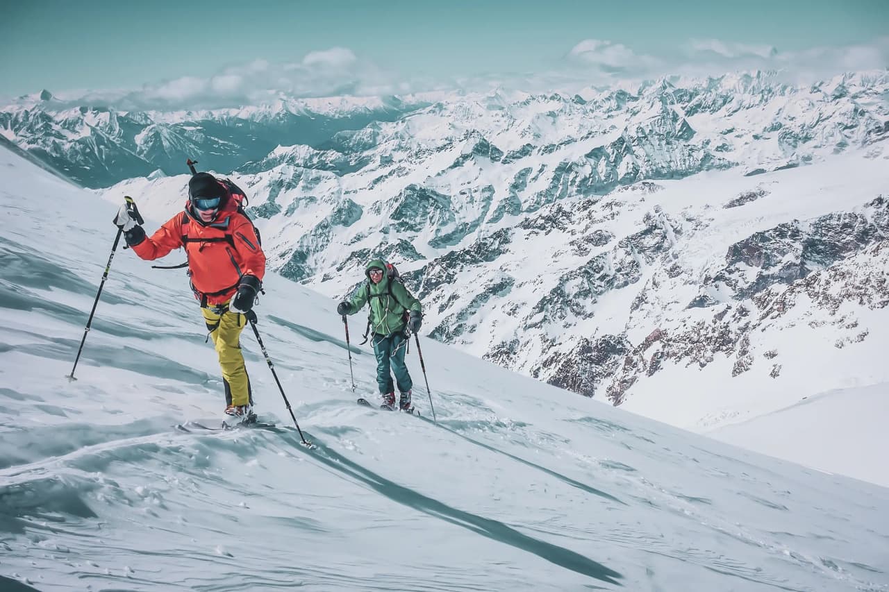 Skiers advancing on snow-covered slopes, with majestic peaks in the background.
