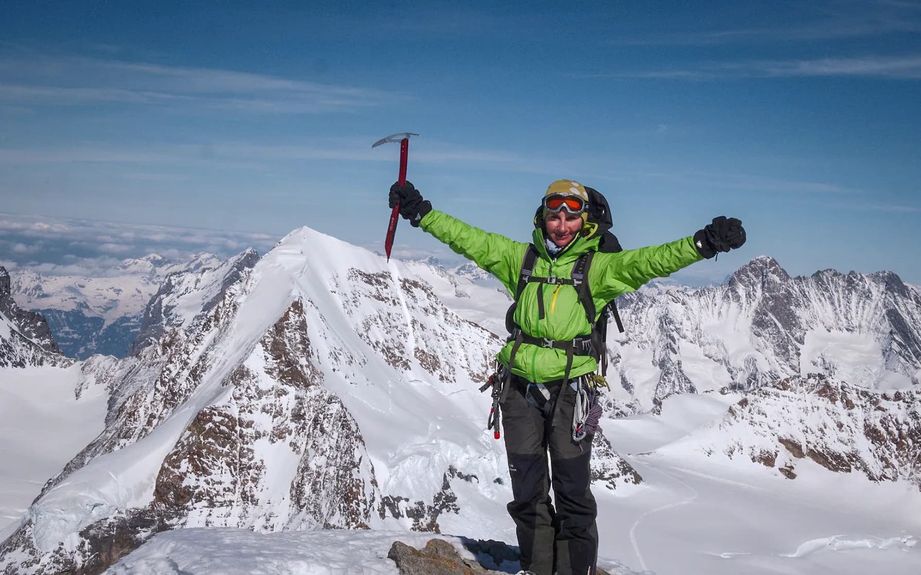 A climber stands at the top of a snow-covered mountain, arms raised in victory.