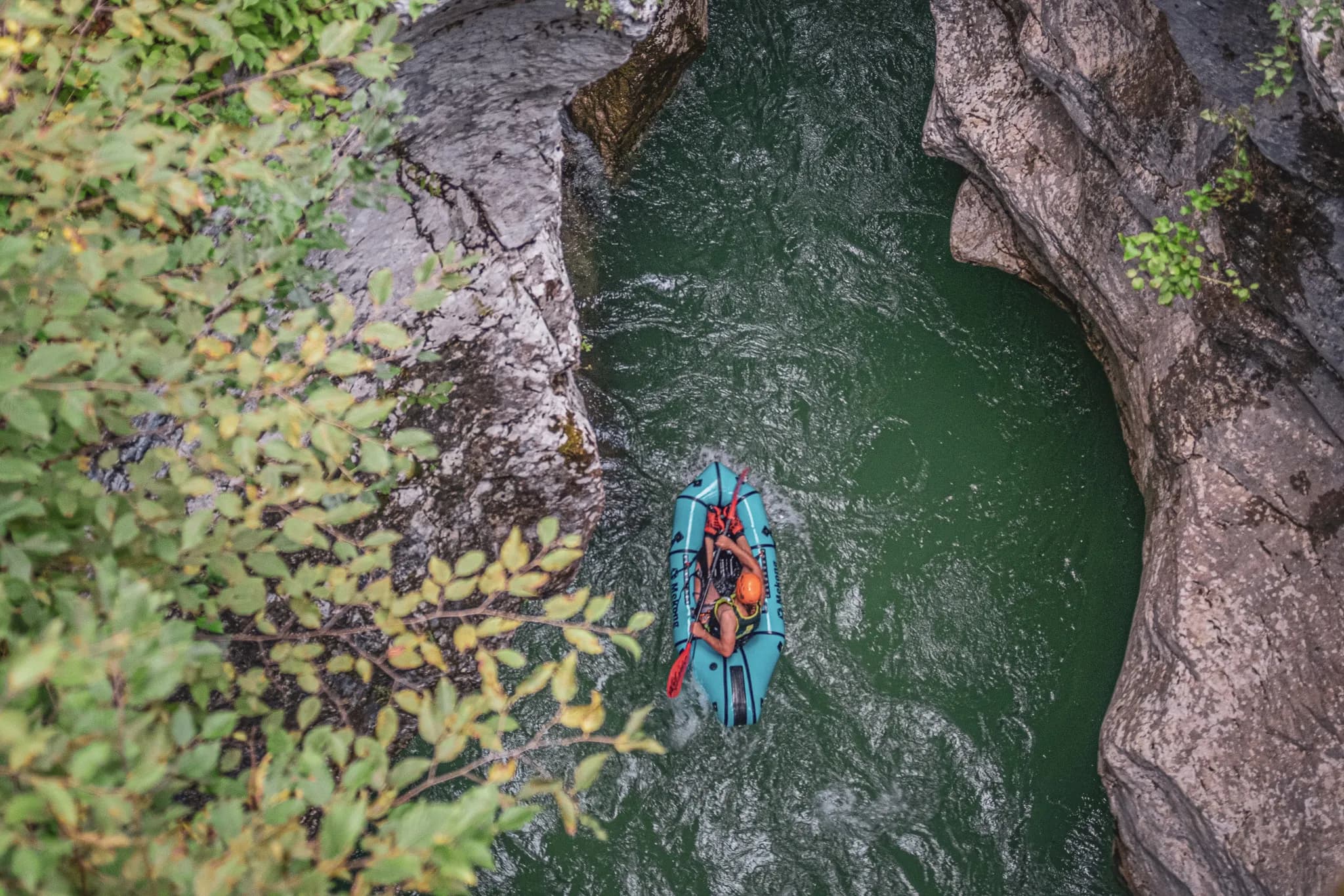 Un packraft glisse sur une rivière verte entourée de falaises et de feuillage luxuriant.