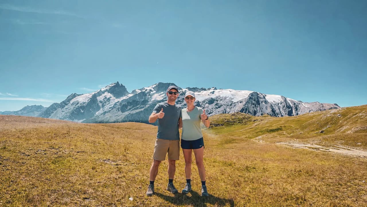 Couple souriant en pleine nature, avec des montagnes majestueuses en arrière-plan.