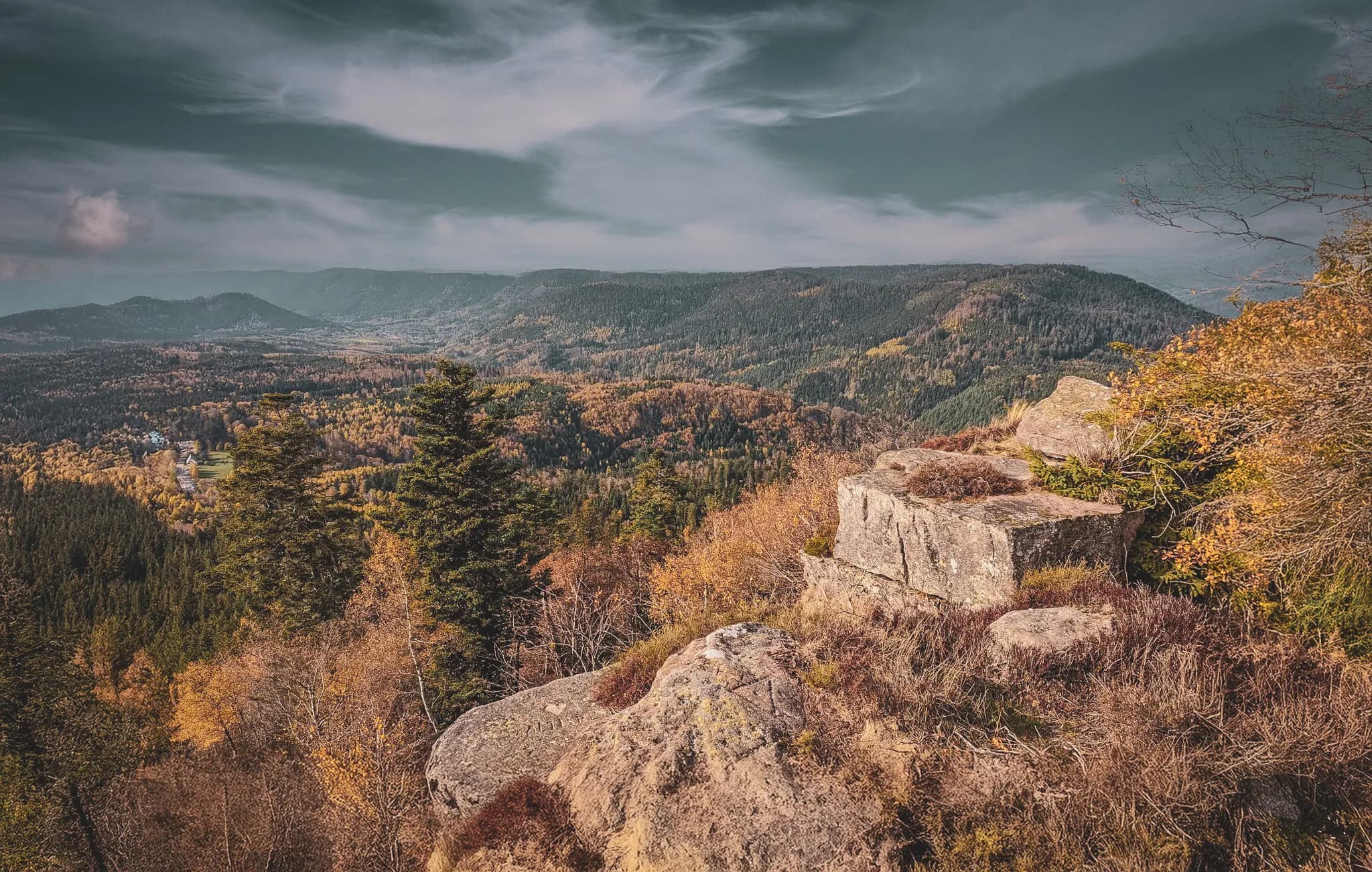 Vue panoramique des Vosges en automne, avec des collines verdoyantes et des rochers majestueux.