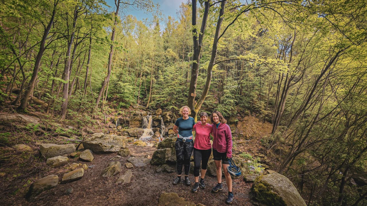 Drie lachende vrienden voor een waterval, omringd door groen in de Hoge Venen.