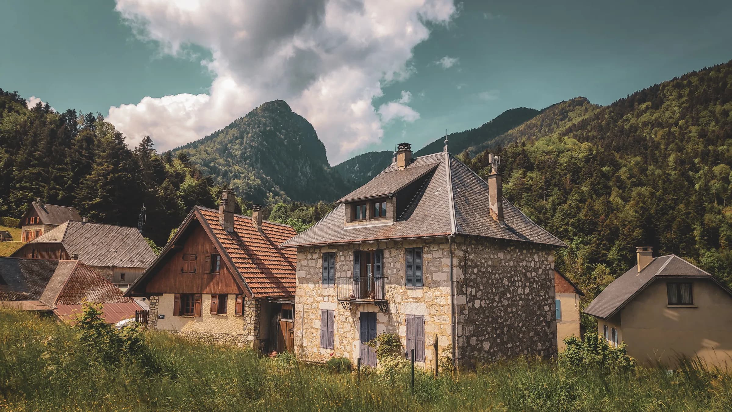 Charmantes maisons en pierre, écrin de verdure, avec les sommets des Chartreux en arrière-plan.