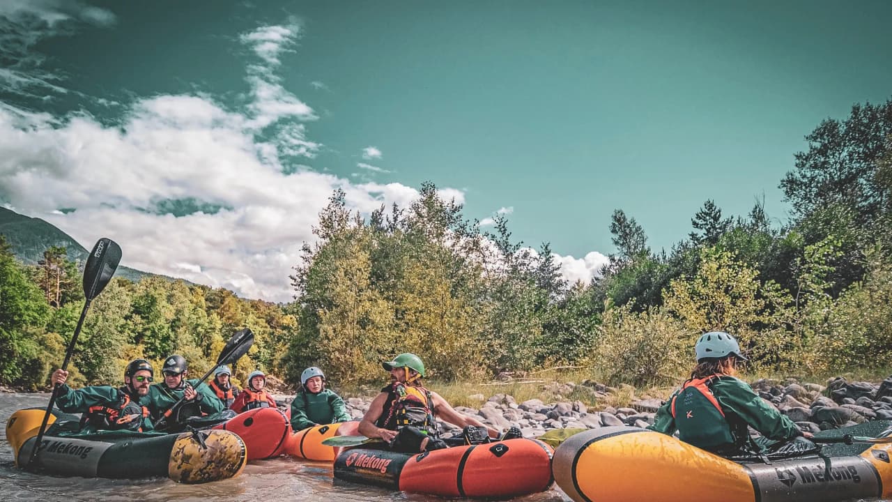 Een groep packrafters op de rivier, omringd door bergen en groen, in een gezellige sfeer.