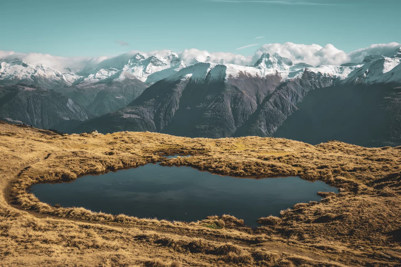 A spectacular Alpine panorama with a serene lake and snow-capped mountains in the background.
