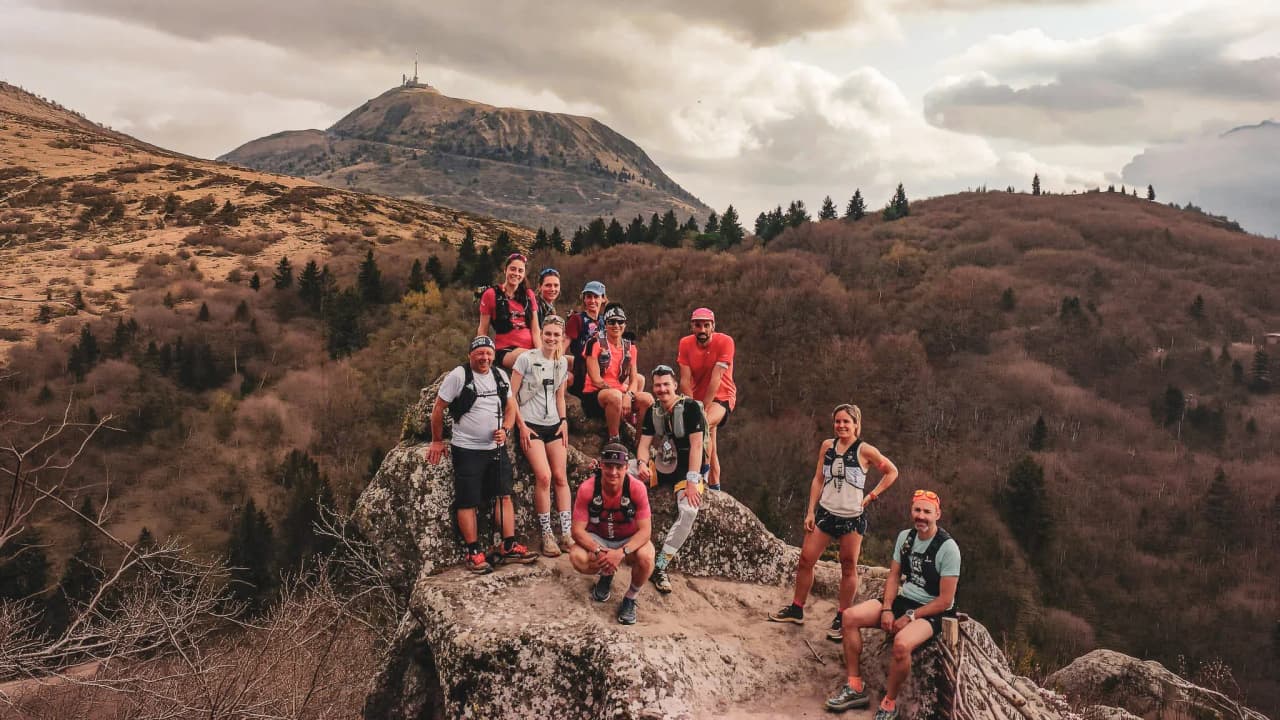 A group of athletes on a steep summit, with majestic volcanoes in the background.