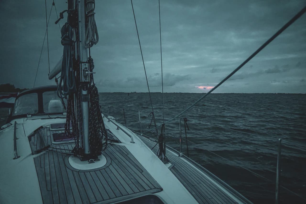Een zeilboot varend op rustig water onder een bewolkte hemel in de schemering in Zeeland.
