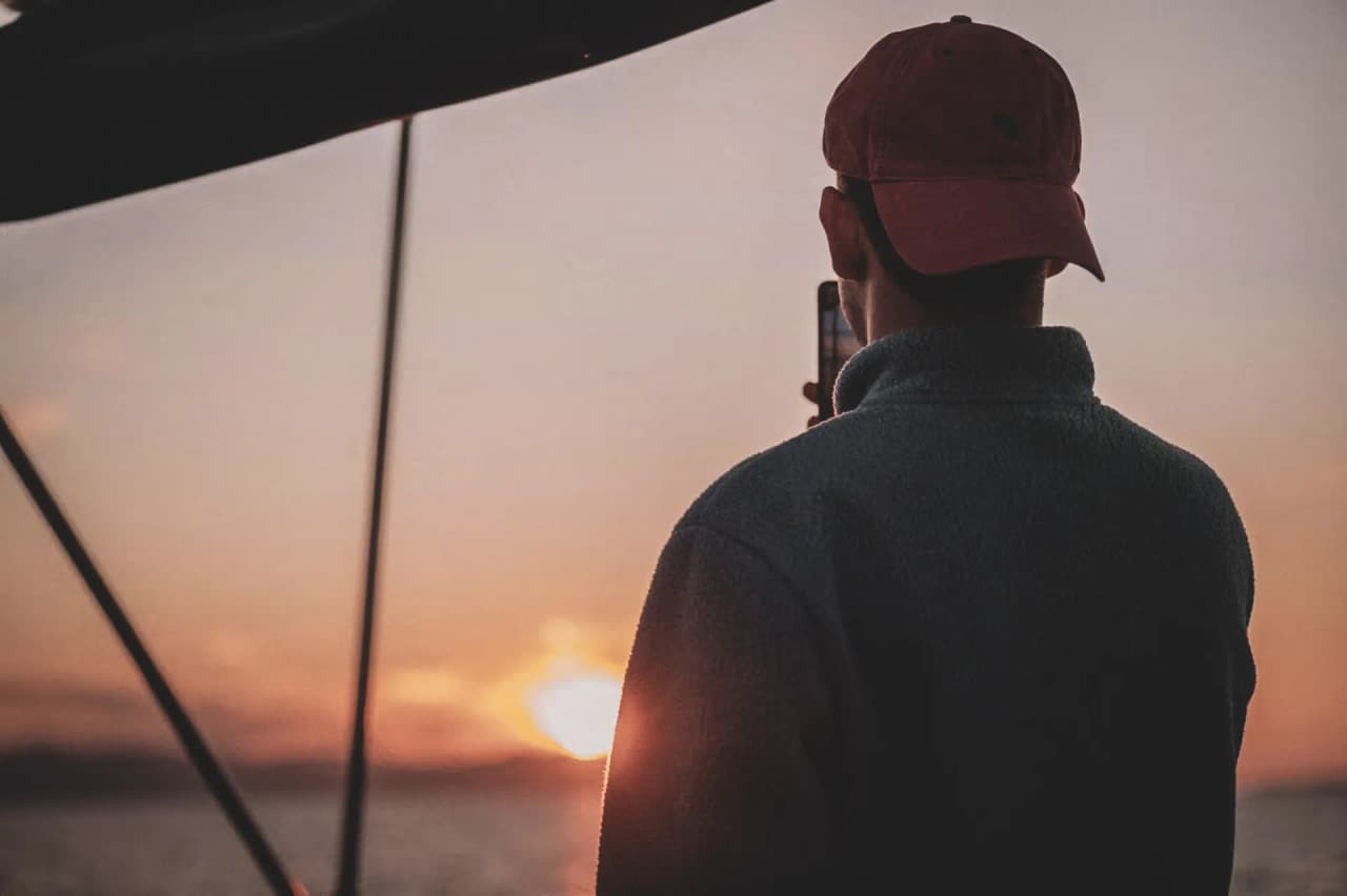 Un voyageur admirant un coucher de soleil en mer, smartphone à la main, une ambiance apaisante.