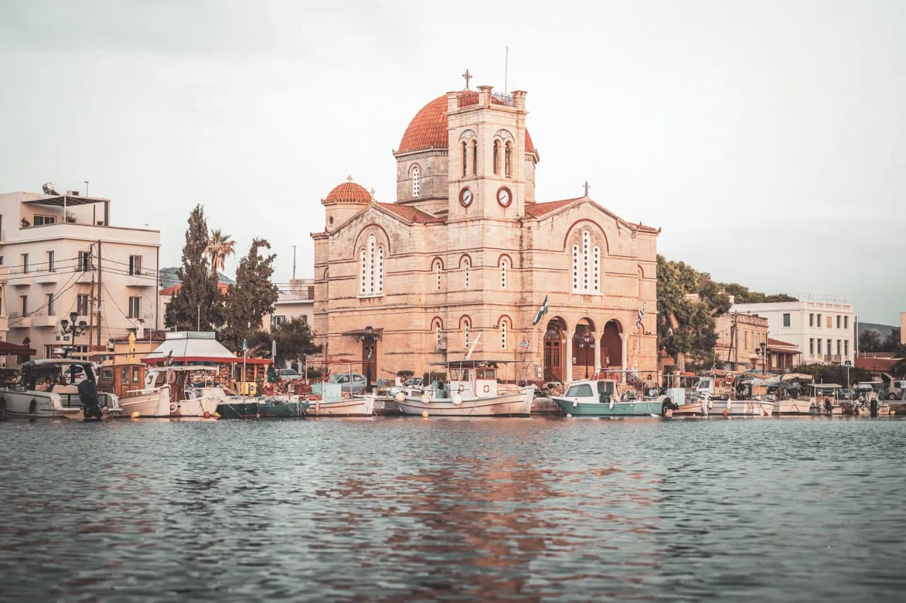 Église pittoresque au bord de la mer, bateaux colorés au port, atmosphère méditerranéenne.
