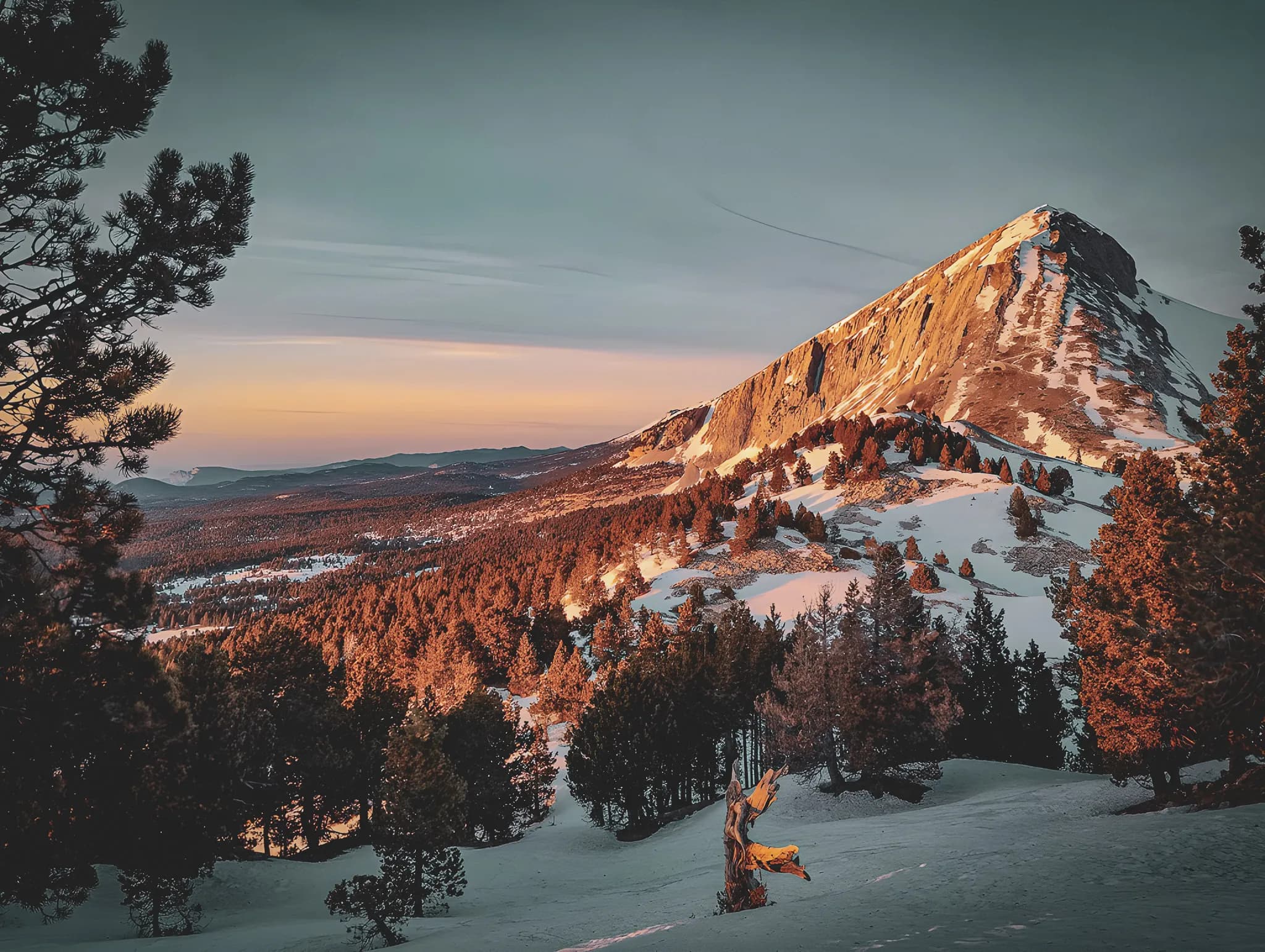 Een majestueuze berg onder een schemerige hemel, omringd door bossen en sneeuw, een uitnodiging tot avontuur.