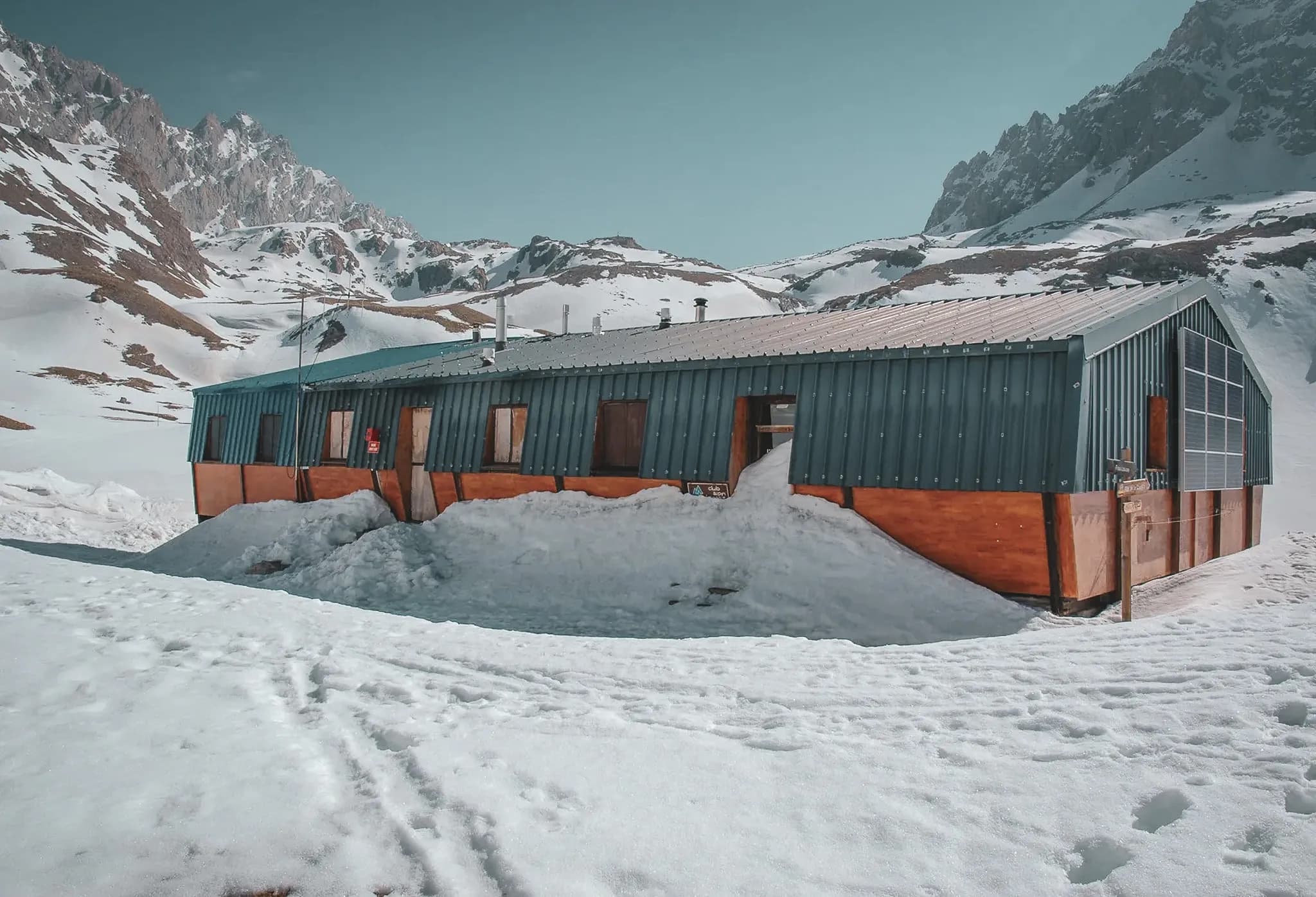 Een houten Berghut omringd door sneeuw, met majestueuze bergen op de achtergrond, een uitnodiging tot avontuur.