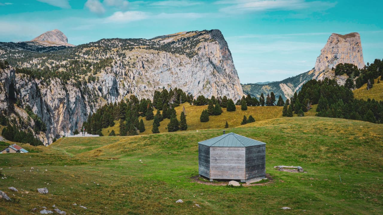 Un chalet en bois posé sur un pâturage verdoyant, entouré de majestueuses falaises et forêts.
