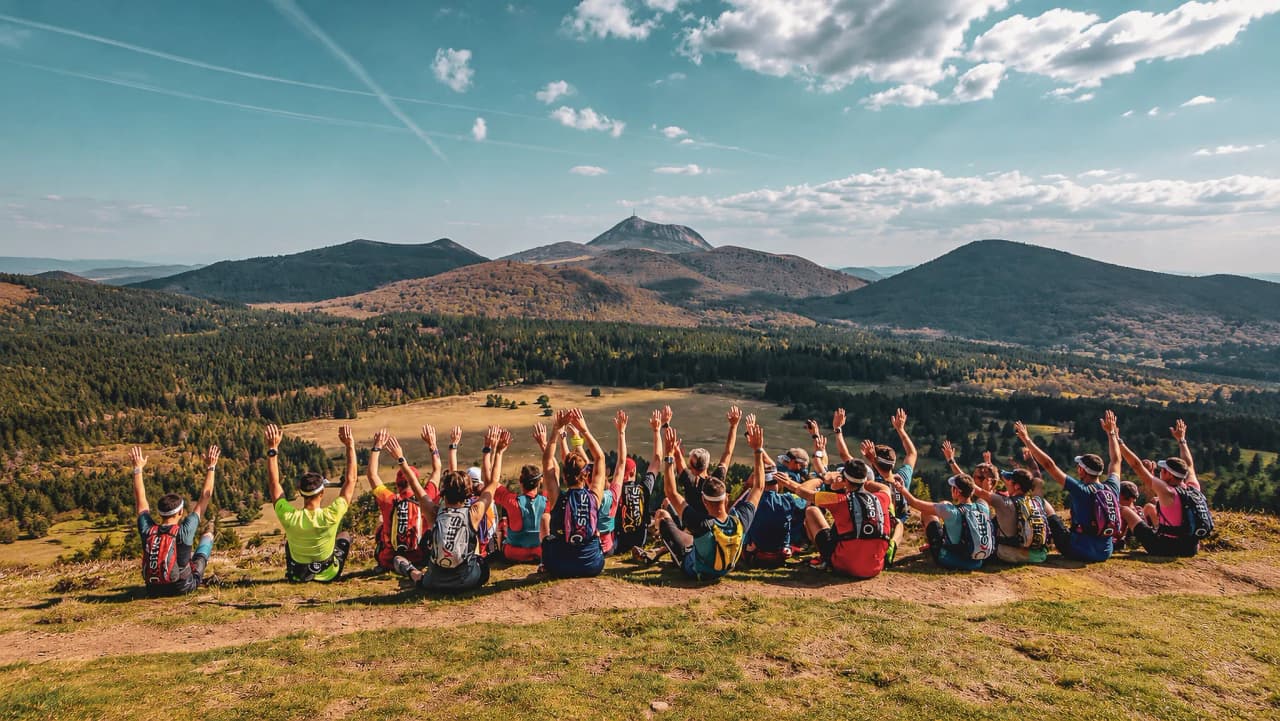 A group of trail runners raise their arms in front of a breathtaking volcanic panorama in the Auvergne.
