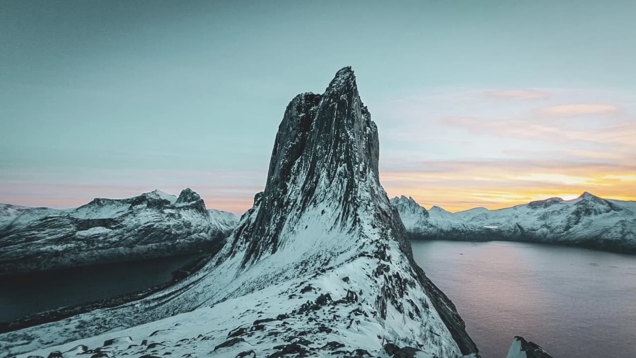 A majestic snow-capped mountain overlooking a fjord, illuminated by a colourful sky at dusk.