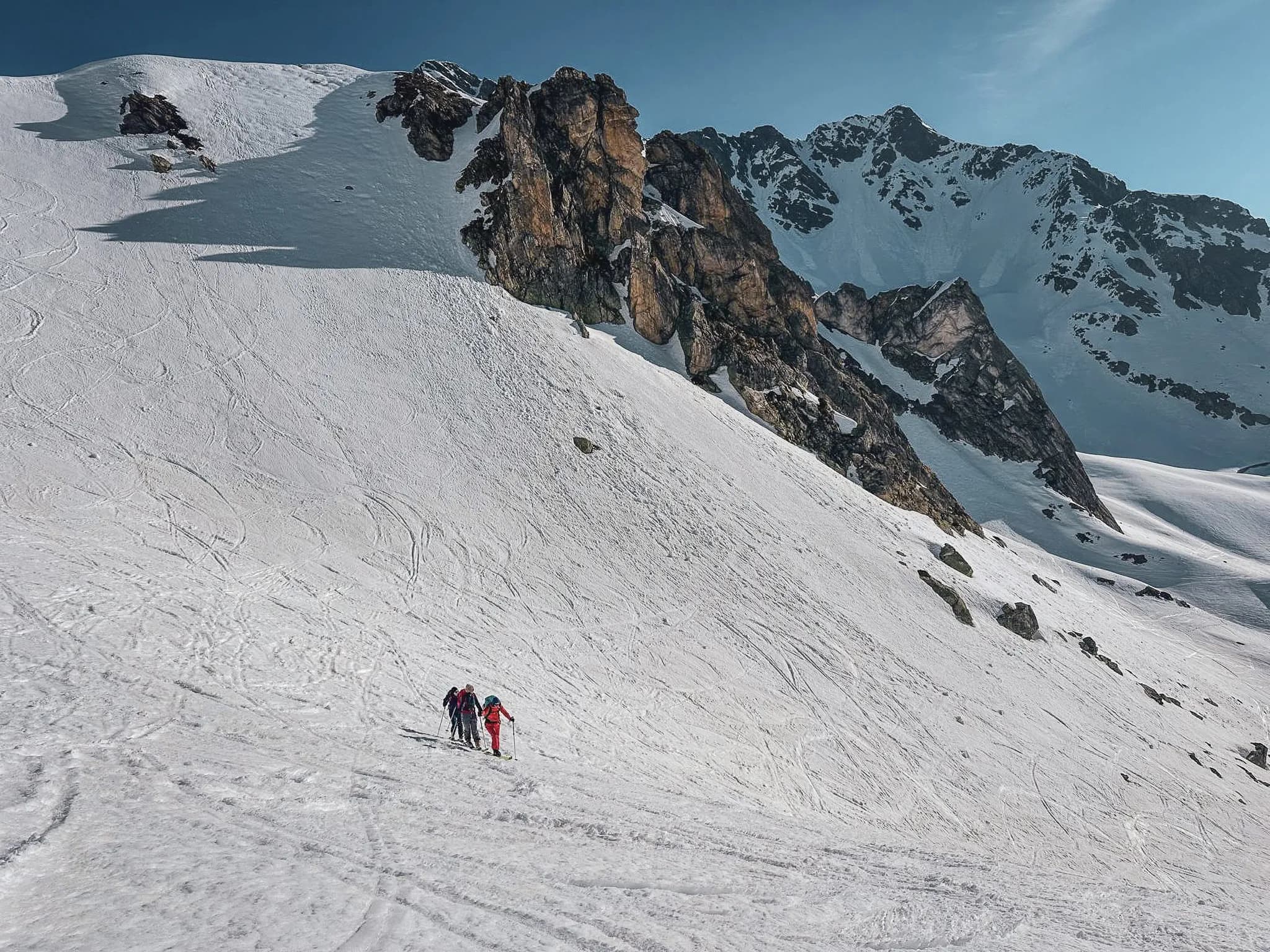 Three skiers set off across a vast expanse of immaculate snow, surrounded by majestic Alpine mountains.