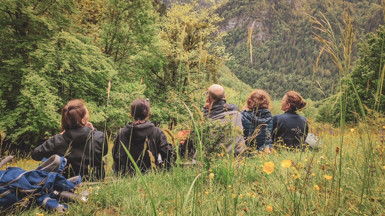 A group sitting on the grass, admiring the lush greenery of the Hautes Bauges.