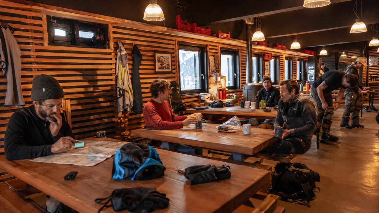 Groupe de randonneurs se préparant autour d'une table en bois dans un refuge chaleureux.
