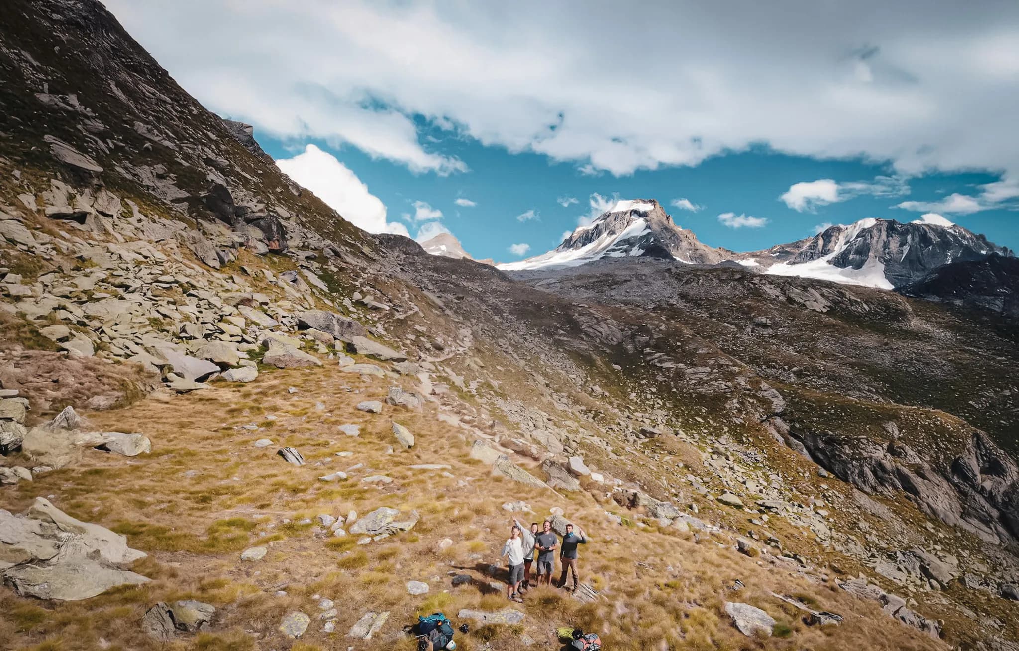 Vier personen staan bij de Victor Emmanuel-hut in het natuurpark Gran Paradiso, omringd door rotsen en gras. Op de achtergrond majestueuze bergen, deels bedekt met sneeuw.