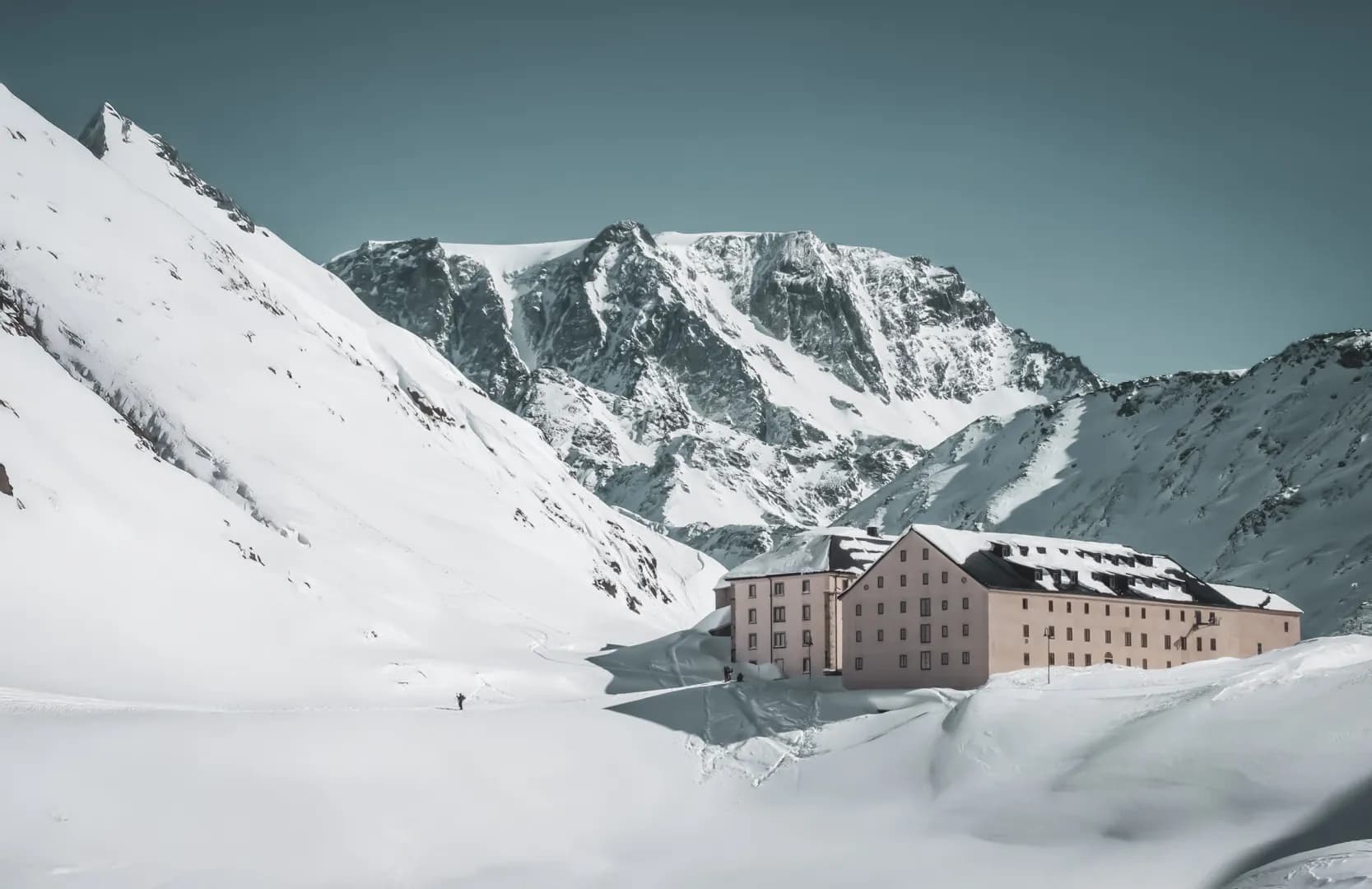 Een okerkleurig Berghut staat majestueus in een besneeuwd landschap, omringd door Alpengebergte.