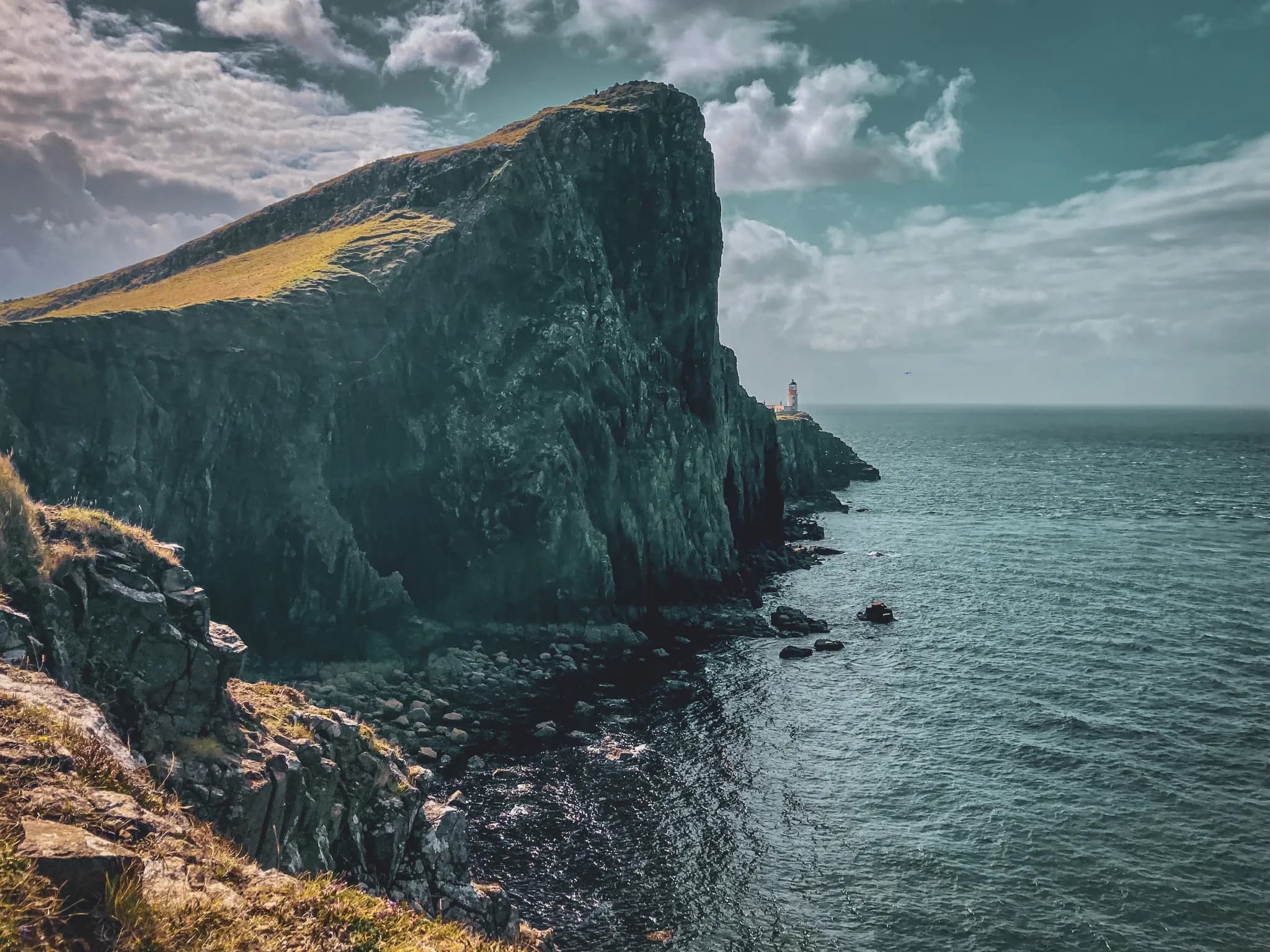 Spectacular cliffs lining the ocean, with a picturesque lighthouse on the Isle of Skye.