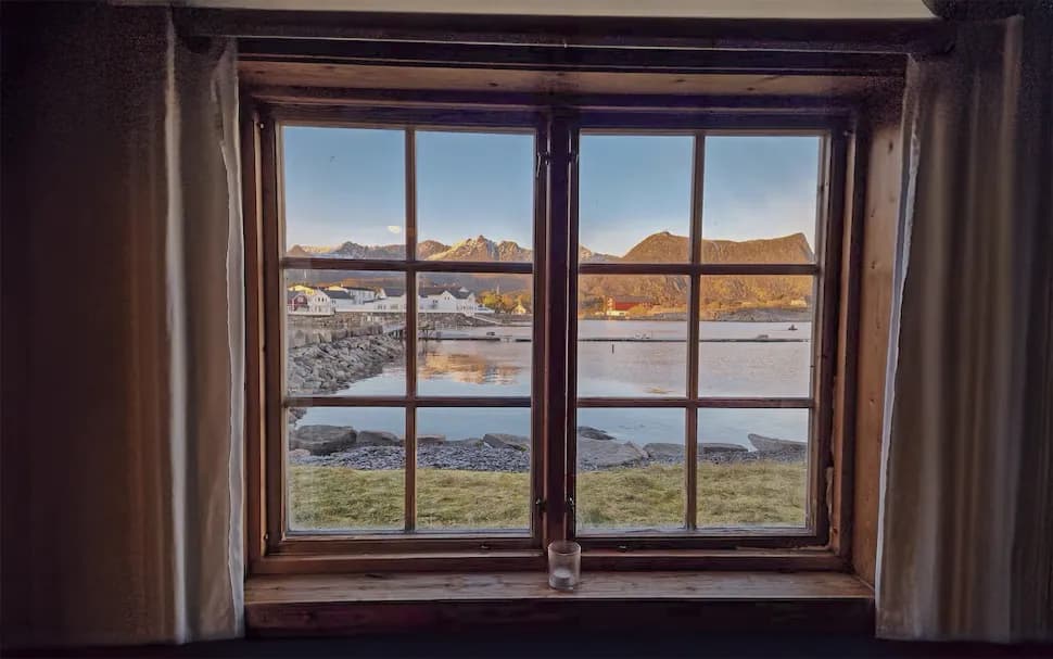 Panoramic view of the Lofoten Islands through a window, with mountains and calm water.