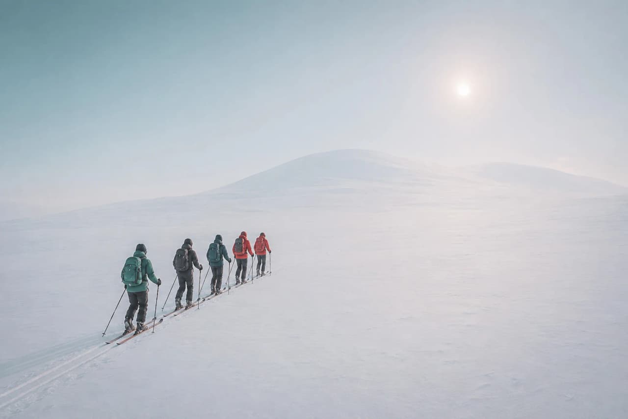 Een groep skiërs die door een besneeuwd landschap trekt onder een heldere hemel. Een winteravontuur in Tromsø.