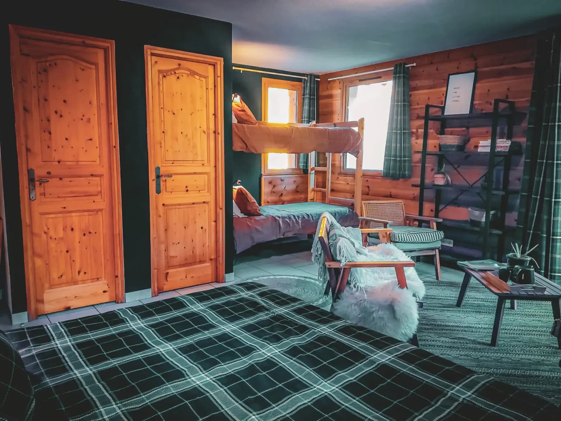 Une chambre accueillante avec des murs en bois clair et des portes en bois massif. Deux lits superposés sont placés contre un mur, tandis qu'un lit simple est également présent. Des rideaux à carreaux encadrent les fenêtres,