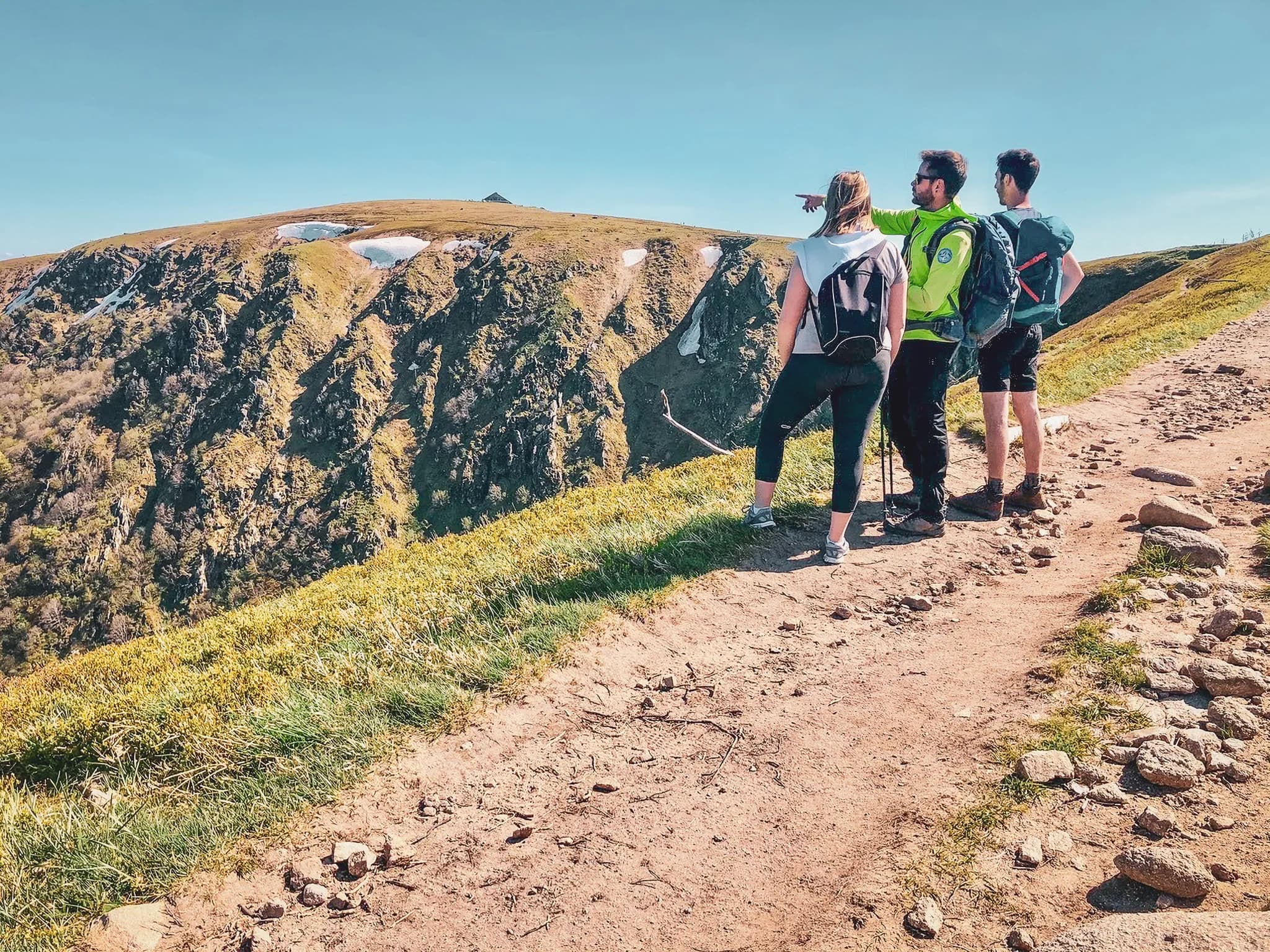 Trois randonneurs admirent le paysage montagneux des Vosges par une belle journée ensoleillée.