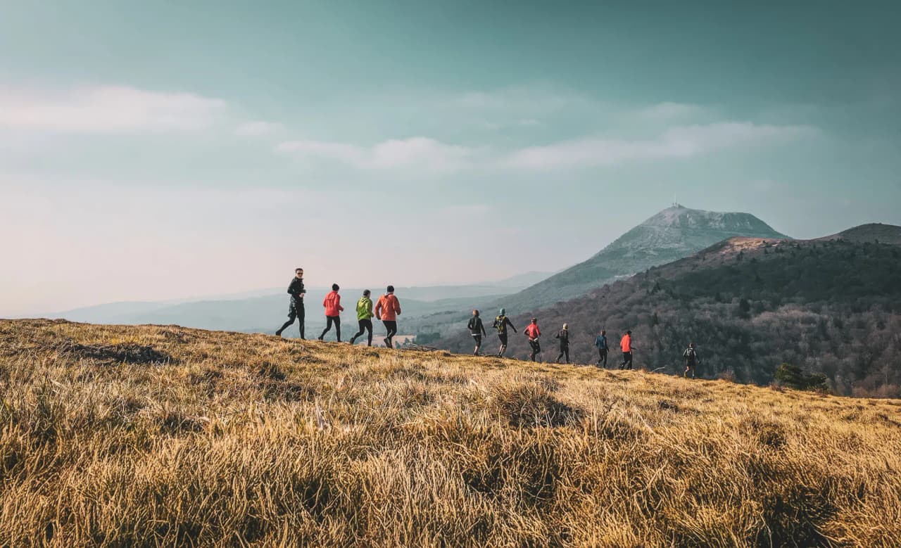 A group of runners cross golden meadows with volcanic mountains in the background.