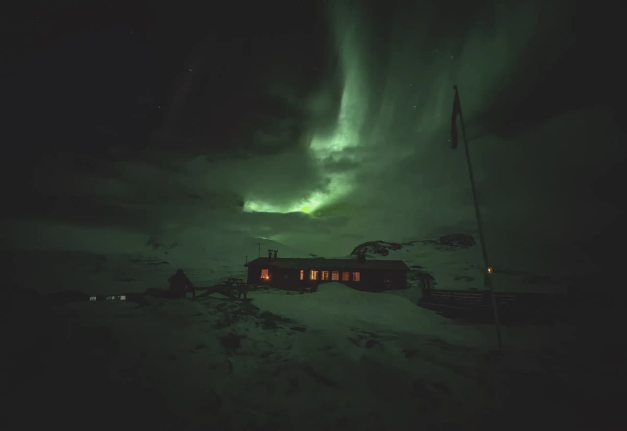 A luminous Mountain hut under the brilliant Northern Lights in Swedish Lapland.