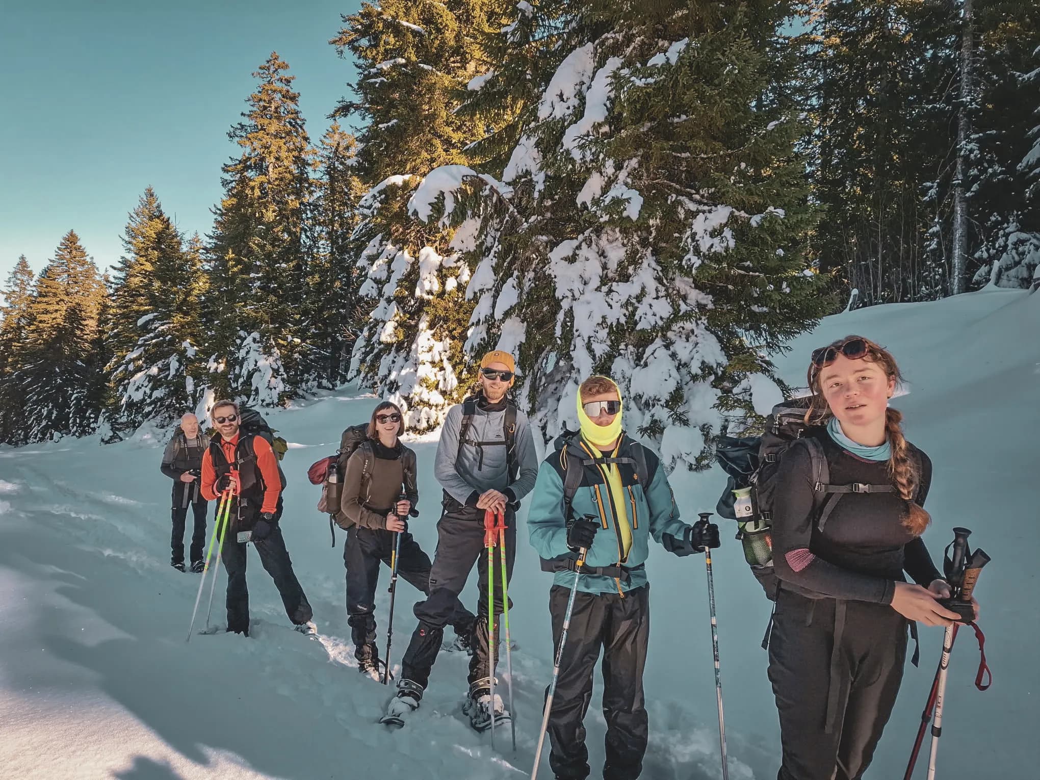 Groupe en raquettes, découvrant les paysages enneigés du Jura suisse, sous un ciel ensoleillé.