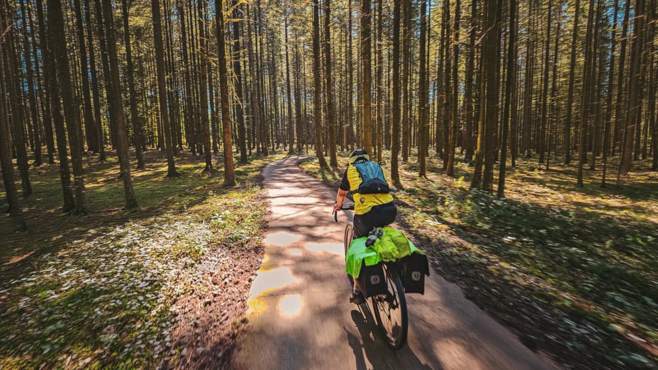 Cyclist on a dirt road through golden fields, under a sunny blue sky.