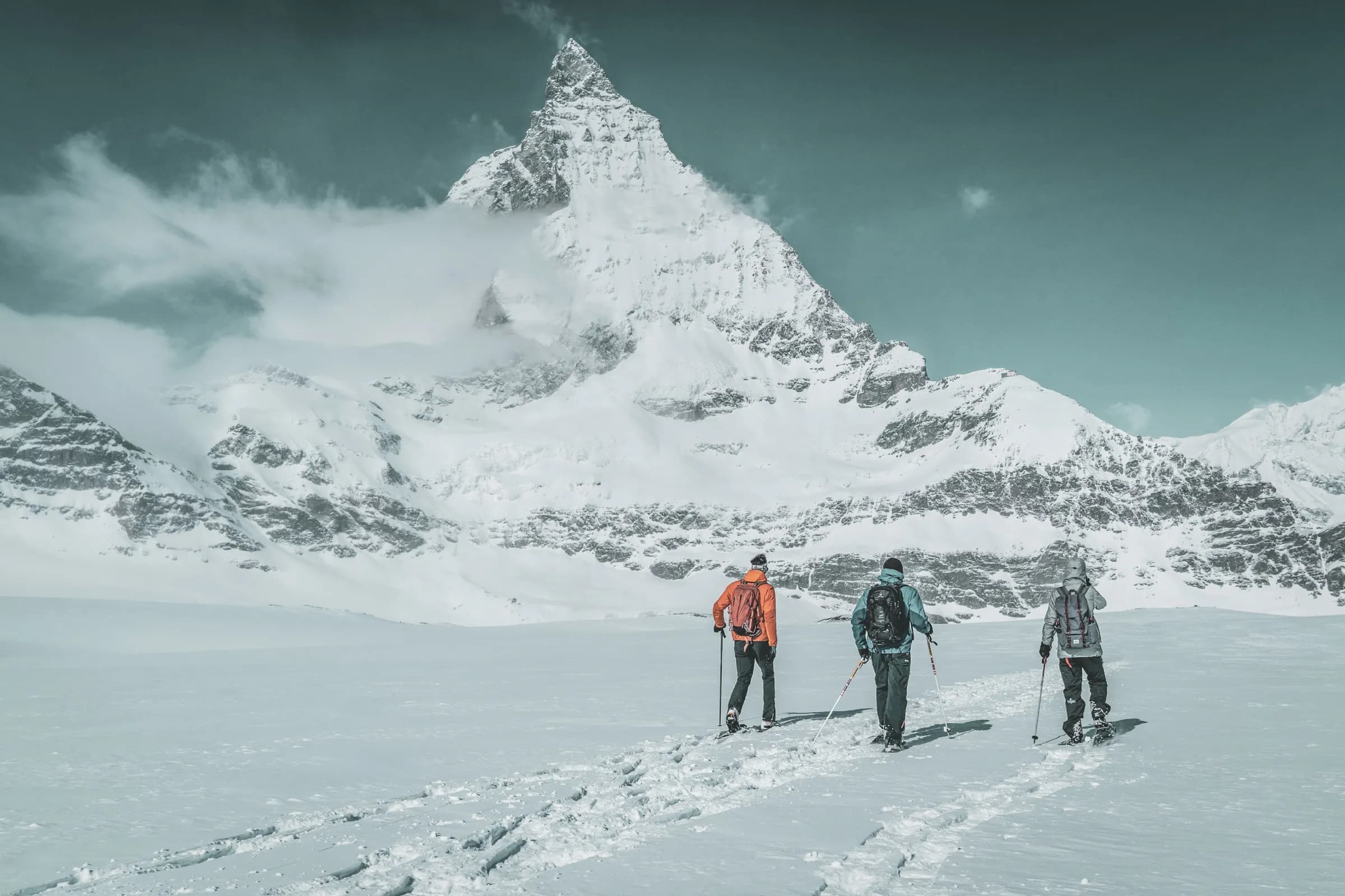 Trois skieurs explorent un glacier sous un majestueux sommet enneigé, ambiance alpine sauvage.