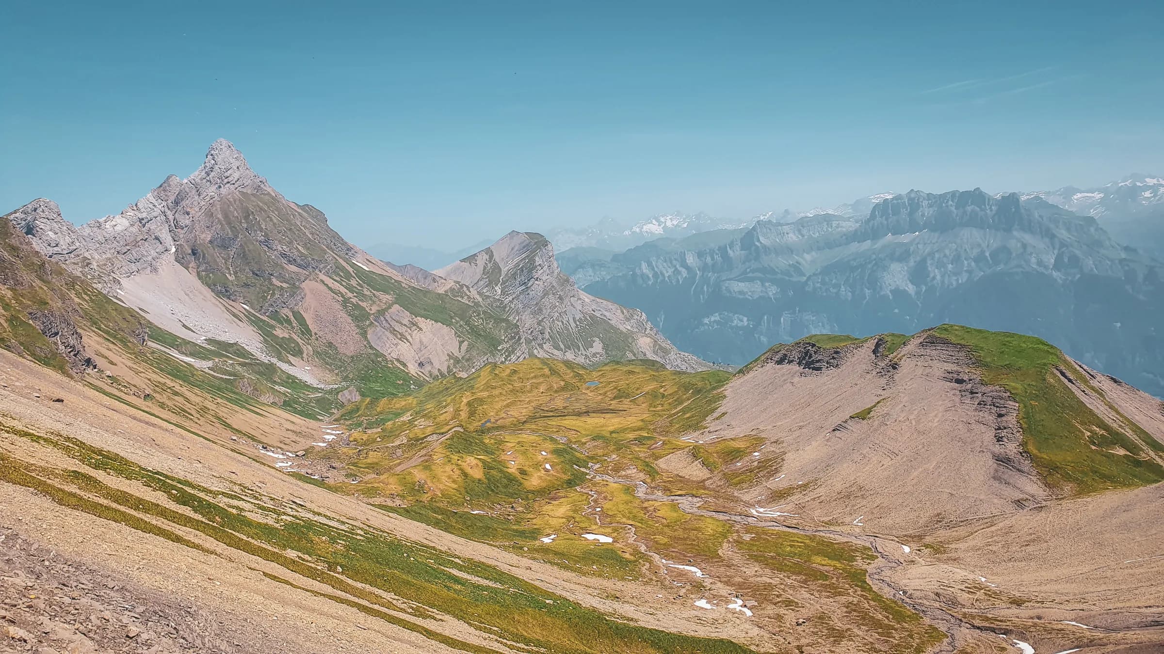 Panoramic views of the Aravis, majestic mountains and lush green valleys under a blue sky.