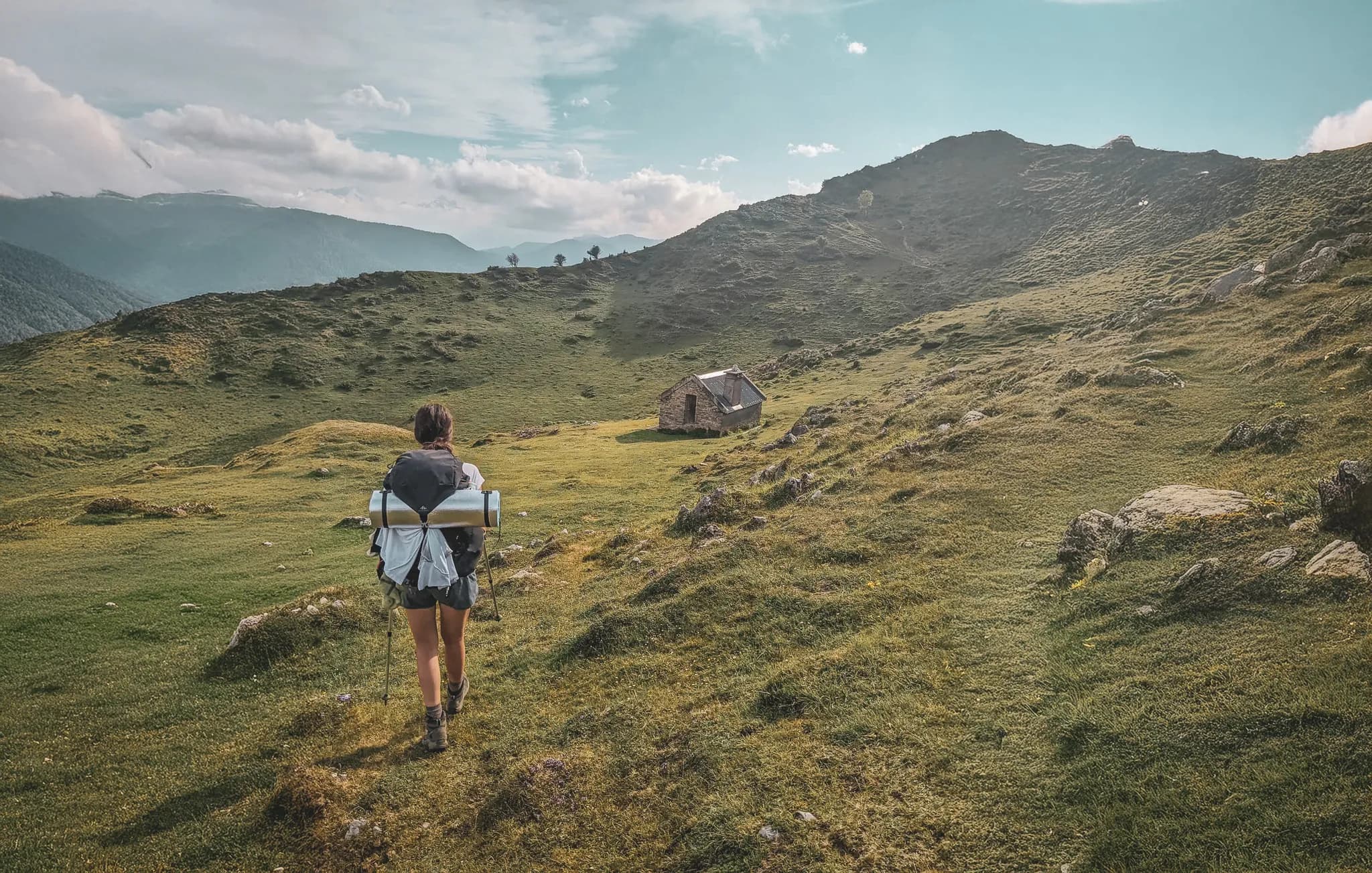 Randonneuse sur un sentier verdoyant des Pyrénées, aux paysages sauvages et sereins.